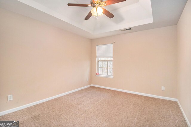 carpeted spare room with a tray ceiling and ceiling fan