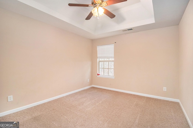 empty room featuring carpet floors, a tray ceiling, visible vents, ceiling fan, and baseboards