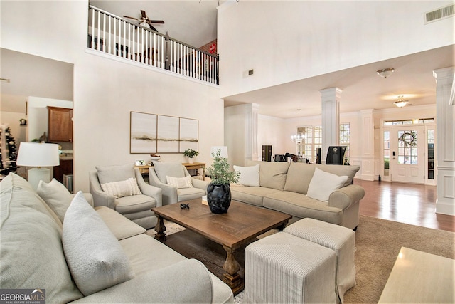 living room featuring ceiling fan with notable chandelier, a towering ceiling, ornamental molding, wood-type flooring, and decorative columns