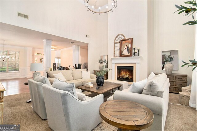 living room with light wood-type flooring, a towering ceiling, ornate columns, and a notable chandelier