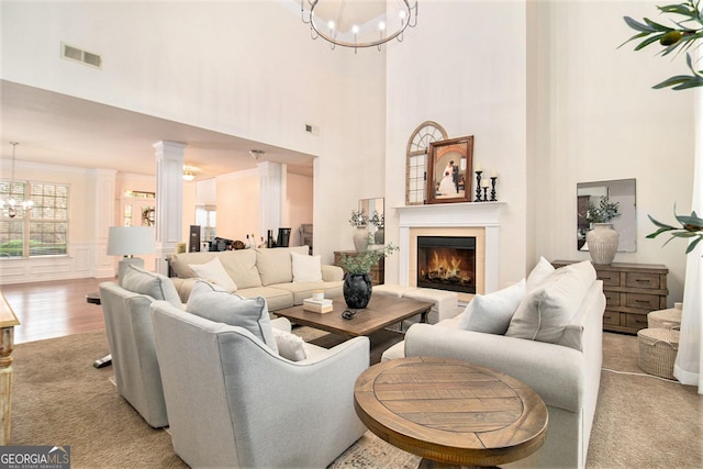 living area with visible vents, a notable chandelier, a lit fireplace, and decorative columns