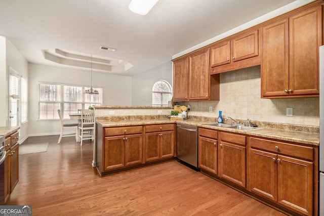 kitchen with dishwasher, brown cabinets, a peninsula, a tray ceiling, and a sink