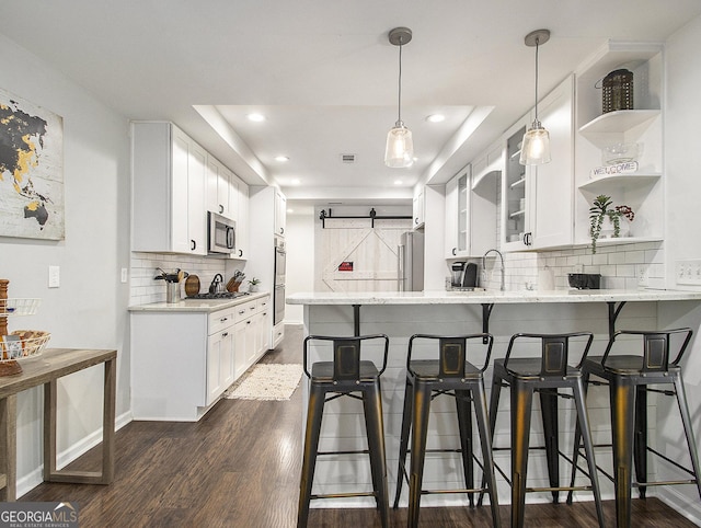 kitchen with pendant lighting, kitchen peninsula, appliances with stainless steel finishes, white cabinetry, and a breakfast bar area