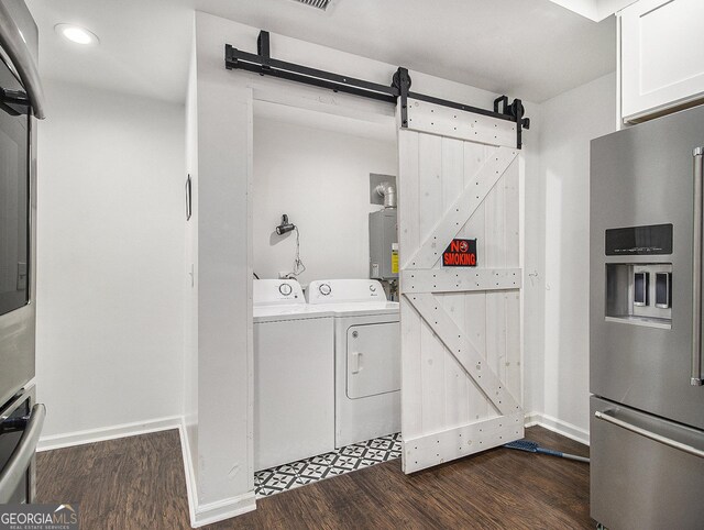 clothes washing area with a barn door, water heater, dark hardwood / wood-style flooring, and independent washer and dryer