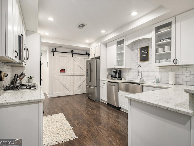 kitchen featuring a barn door, stainless steel appliances, white cabinetry, and light stone counters