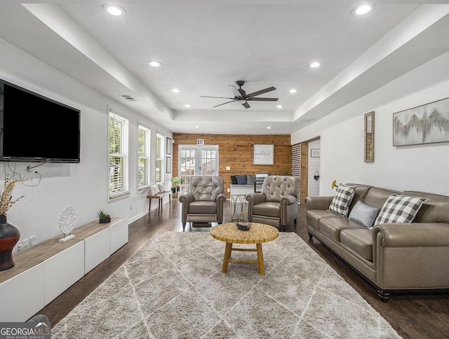 living room with dark hardwood / wood-style floors, ceiling fan, a raised ceiling, and wooden walls