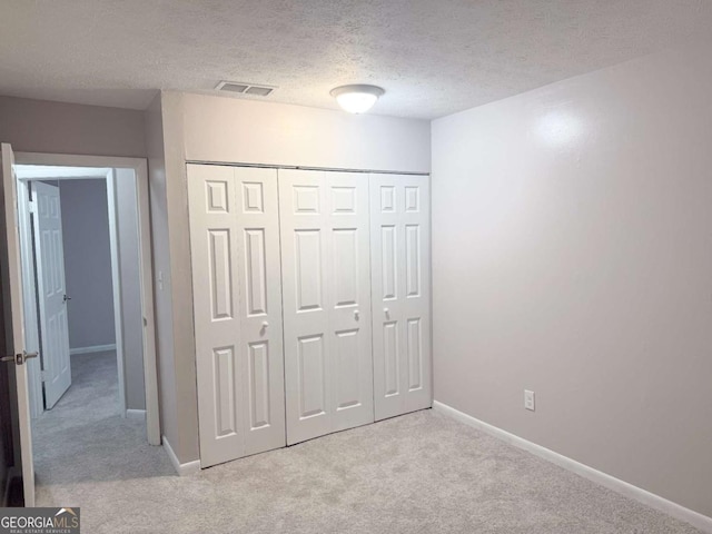 unfurnished bedroom featuring a textured ceiling, light colored carpet, and a closet