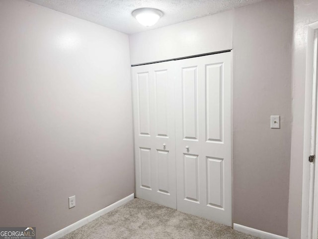 unfurnished bedroom with a textured ceiling, light carpet, and a closet