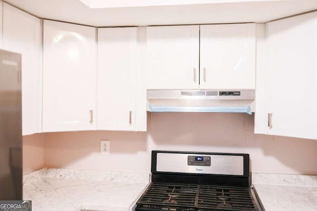 kitchen featuring light stone countertops, stove, and white cabinetry