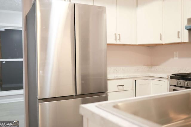 kitchen with ventilation hood, white cabinetry, and stainless steel refrigerator