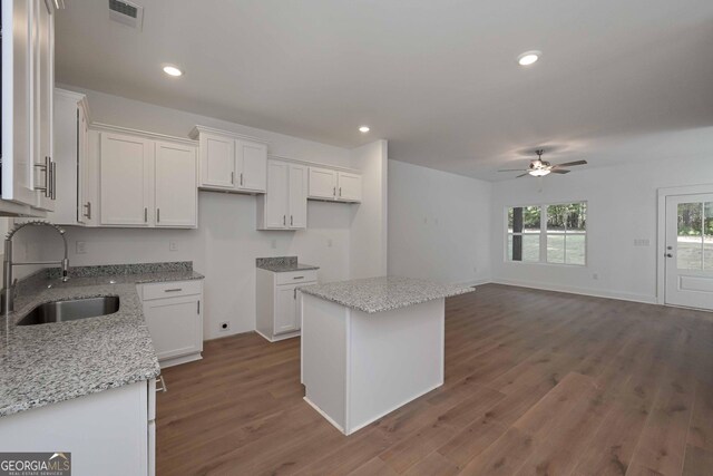 kitchen featuring light stone counters, a sink, white cabinetry, visible vents, and a center island