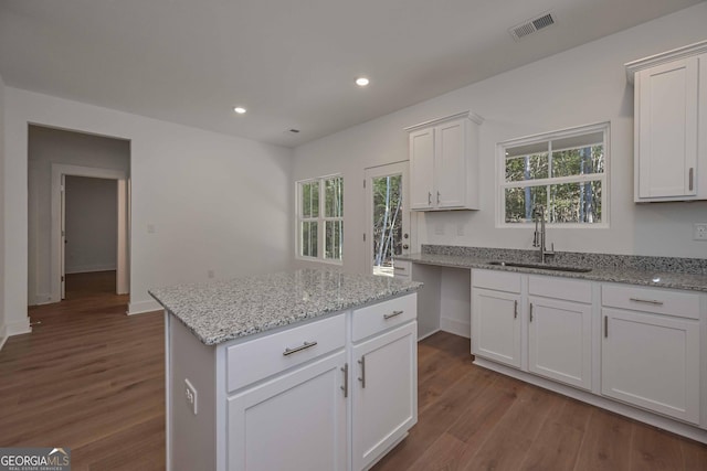 kitchen featuring visible vents, a center island, light stone countertops, white cabinetry, and a sink