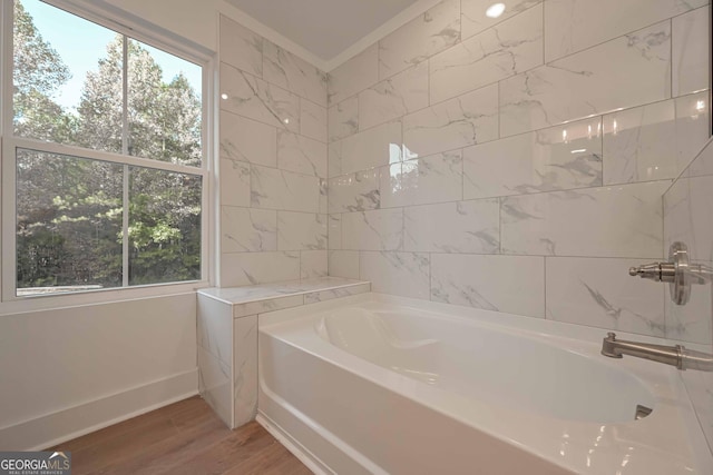 full bath featuring a garden tub, tile walls, ornamental molding, wood finished floors, and baseboards