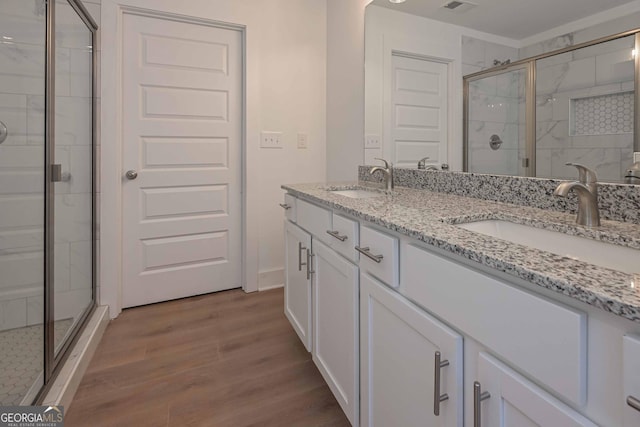 full bath featuring double vanity, wood finished floors, a sink, and a shower stall