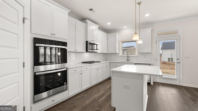 kitchen with appliances with stainless steel finishes, ornamental molding, decorative light fixtures, a center island, and white cabinetry