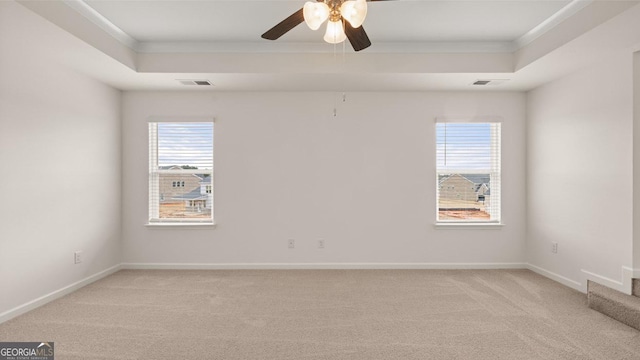 carpeted empty room with a raised ceiling, ceiling fan, and ornamental molding