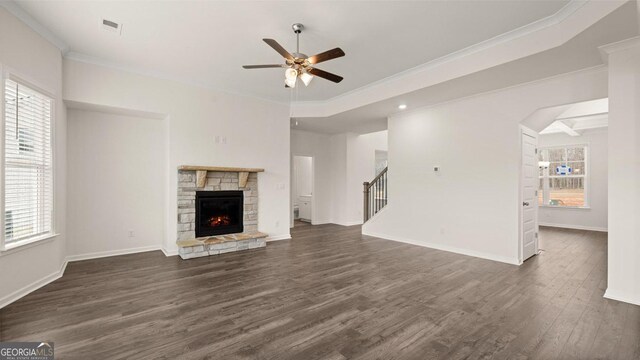 unfurnished living room with dark wood-type flooring, crown molding, a healthy amount of sunlight, and a stone fireplace