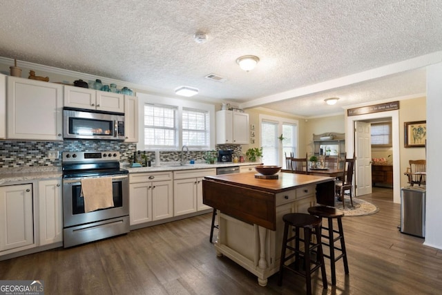 kitchen with white cabinets, appliances with stainless steel finishes, dark hardwood / wood-style floors, and plenty of natural light