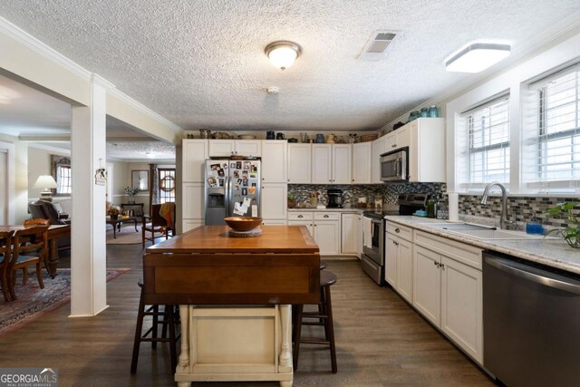 kitchen with white cabinetry, ornamental molding, stainless steel appliances, and dark wood-type flooring