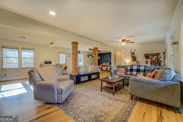 living room with crown molding, wood-type flooring, ceiling fan, and ornate columns