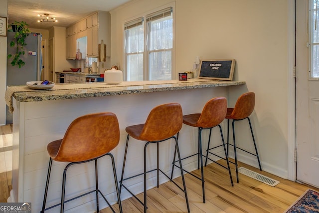 kitchen with a breakfast bar, light brown cabinets, stainless steel fridge, and light wood-type flooring