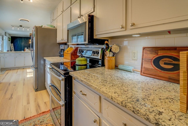 kitchen featuring tasteful backsplash, white cabinetry, appliances with stainless steel finishes, light stone countertops, and light hardwood / wood-style floors