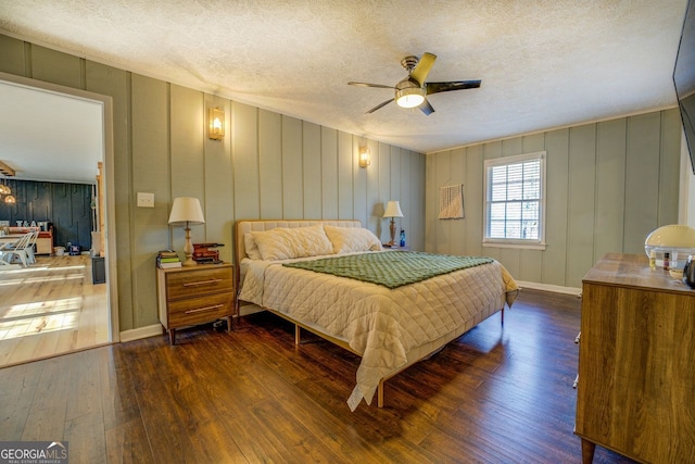 bedroom with wooden walls, ceiling fan, dark hardwood / wood-style floors, and a textured ceiling