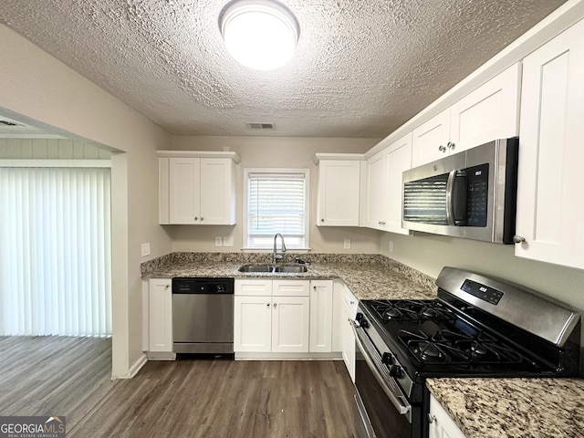 kitchen featuring light stone countertops, appliances with stainless steel finishes, dark wood-type flooring, sink, and white cabinets