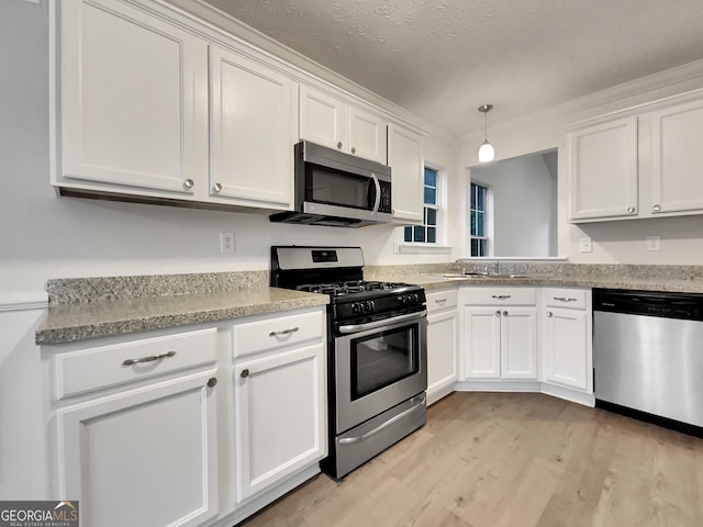 kitchen with light wood-type flooring, a textured ceiling, stainless steel appliances, decorative light fixtures, and white cabinets