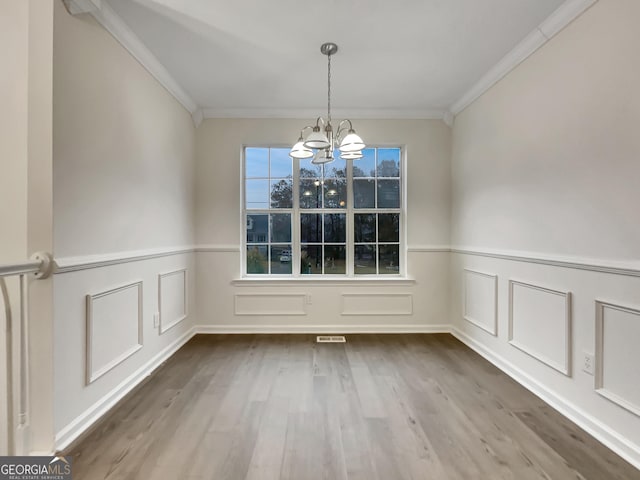 unfurnished dining area with hardwood / wood-style floors, a chandelier, and ornamental molding