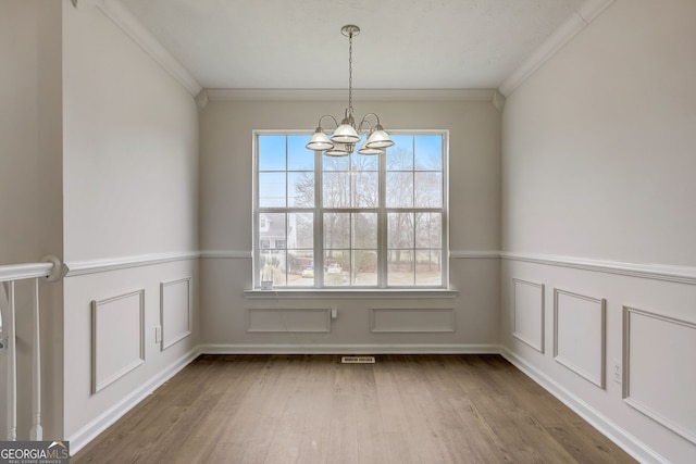 unfurnished dining area featuring ornamental molding, hardwood / wood-style flooring, and a notable chandelier