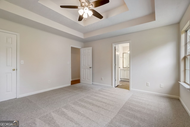 unfurnished bedroom with ceiling fan, light colored carpet, ensuite bathroom, and a tray ceiling