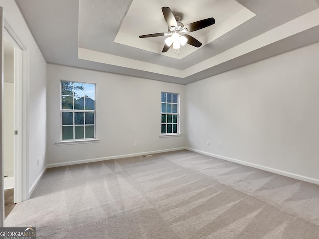 carpeted spare room with a tray ceiling and ceiling fan