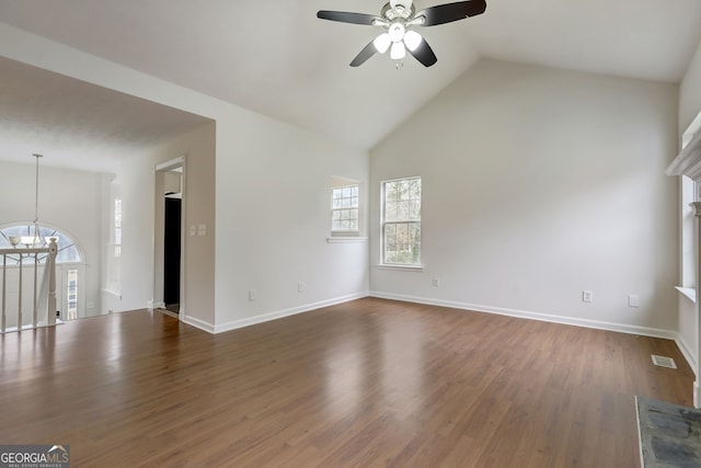 unfurnished living room featuring ceiling fan with notable chandelier, a stone fireplace, dark wood-type flooring, and high vaulted ceiling