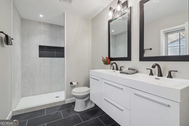 bathroom with tile patterned flooring, vanity, tiled shower, and toilet