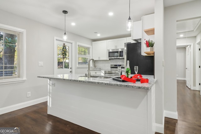 kitchen featuring dark wood-type flooring, stainless steel appliances, light stone counters, decorative light fixtures, and white cabinets