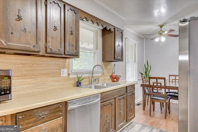 kitchen with appliances with stainless steel finishes, backsplash, ornamental molding, sink, and light hardwood / wood-style flooring