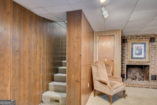 living area with carpet flooring, a drop ceiling, and wooden walls