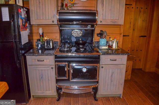 kitchen with dark stone countertops, light wood-type flooring, wooden walls, and black appliances