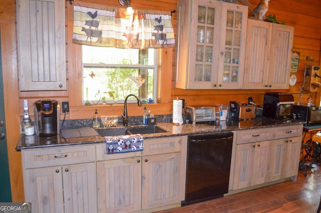 kitchen featuring dishwasher, sink, light hardwood / wood-style flooring, dark stone countertops, and wooden walls