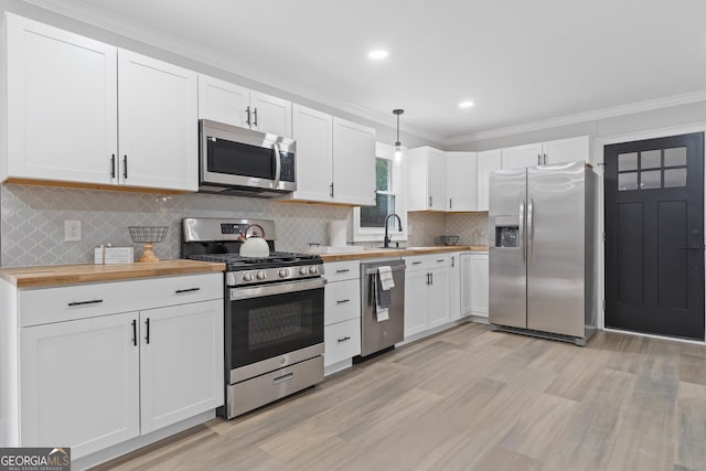 kitchen featuring ornamental molding, butcher block countertops, decorative light fixtures, white cabinetry, and stainless steel appliances