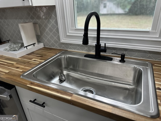 details with wooden counters, backsplash, stainless steel dishwasher, sink, and white cabinetry