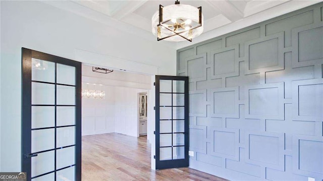 interior space featuring french doors, coffered ceiling, beam ceiling, light hardwood / wood-style flooring, and a notable chandelier