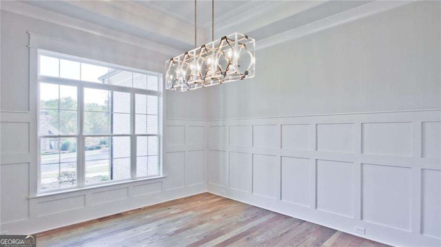 unfurnished dining area with ornamental molding, plenty of natural light, a chandelier, and light hardwood / wood-style flooring