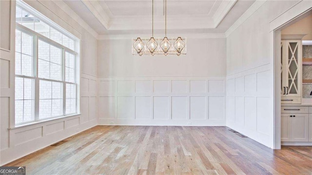 unfurnished dining area with a chandelier, ornamental molding, light hardwood / wood-style floors, and a tray ceiling