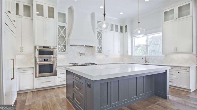 kitchen with dark hardwood / wood-style floors, pendant lighting, white cabinets, custom exhaust hood, and appliances with stainless steel finishes