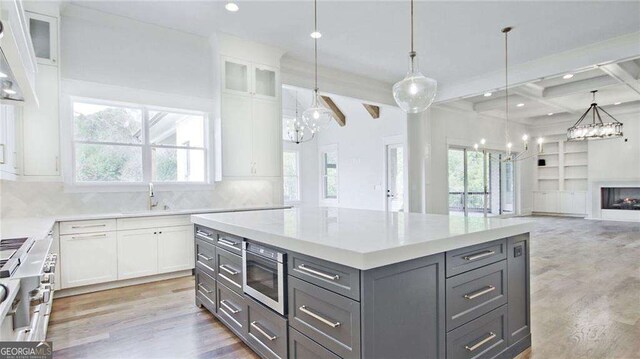 kitchen with appliances with stainless steel finishes, beam ceiling, white cabinets, a kitchen island, and plenty of natural light