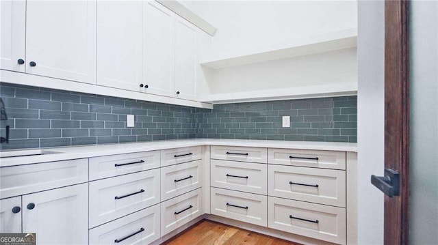 kitchen with backsplash, light hardwood / wood-style floors, white cabinetry, and sink