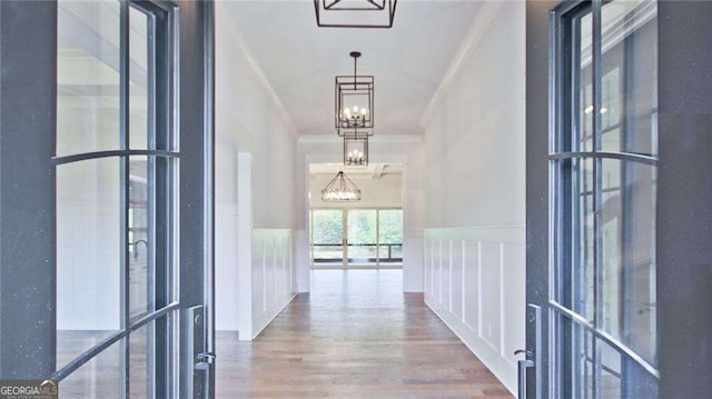 hallway featuring wood-type flooring, crown molding, and an inviting chandelier