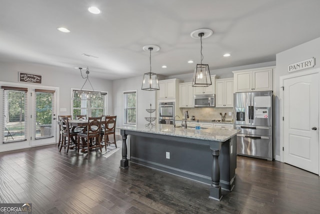 kitchen featuring light stone countertops, stainless steel appliances, dark hardwood / wood-style flooring, pendant lighting, and a kitchen island with sink